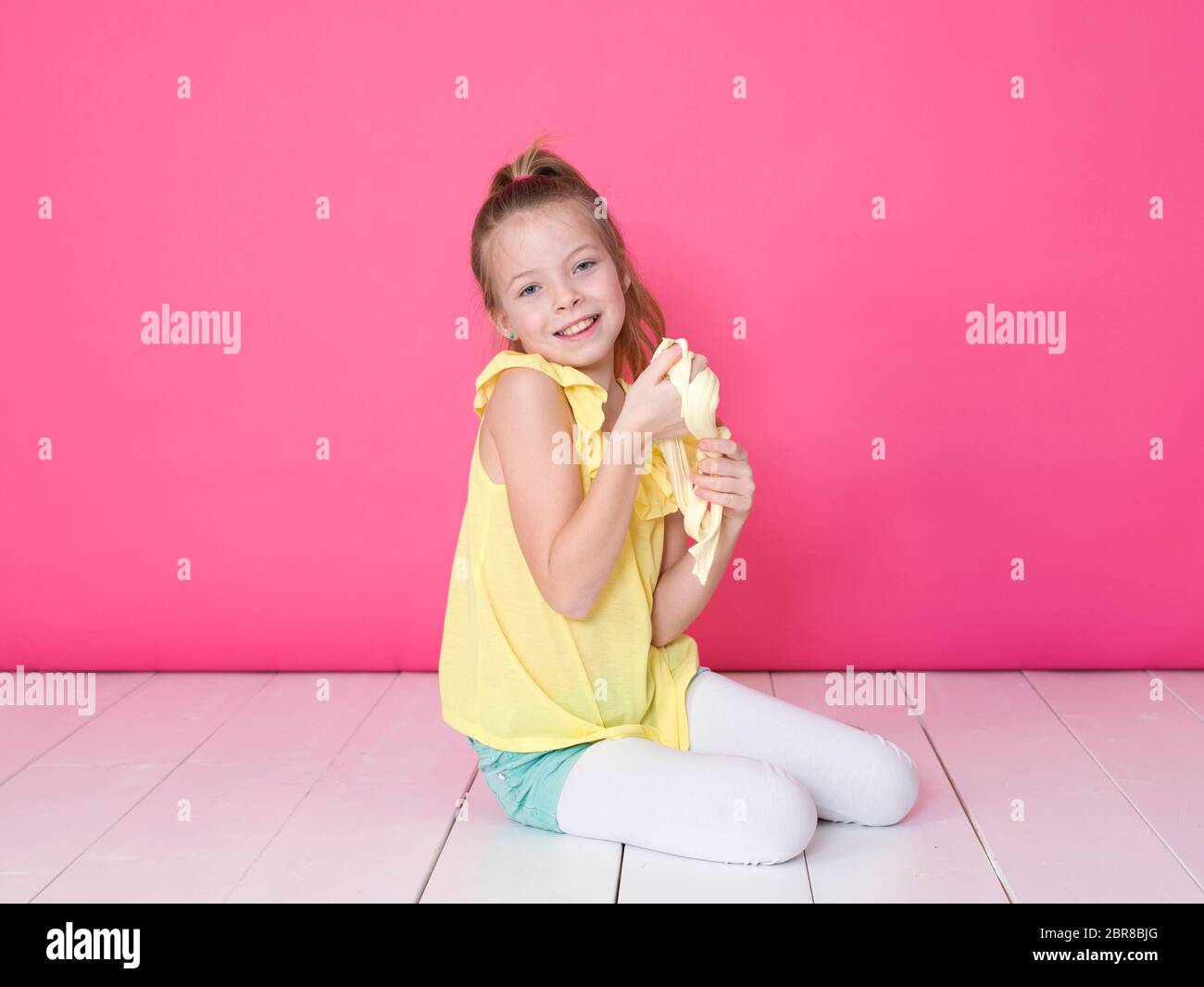 Belle jeune fille de 10 ans joue avec slime jaune en face de fond rose Banque D'Images