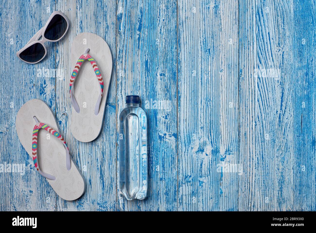 Accessoires de plage : tongs blanches et lunettes de soleil sur fond bleu en bois. Vue de dessus avec espace de copie. Concept de vacances et de voyages en mer. Somme Banque D'Images