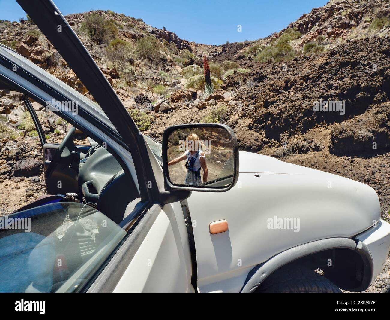 Vue partielle d'une grande voiture, dans le côté droit du miroir est une femme à voir dans l'arrière-plan le paysage désertique aride au pied du Teide en Teneri Banque D'Images