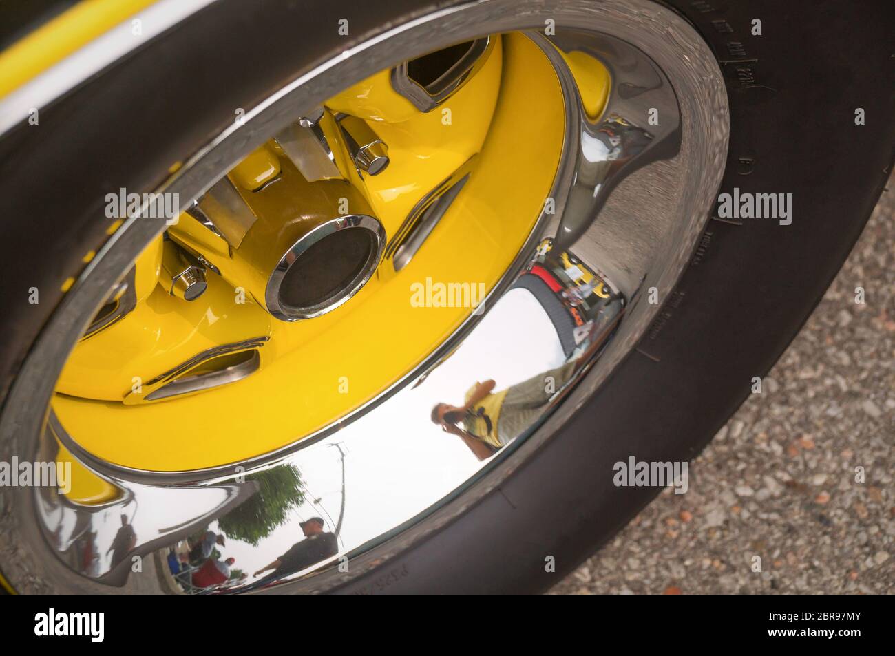 Roue jaune et chromée d'une vieille voiture de sport avec pneu noir reflétant les environs et le photographe Banque D'Images