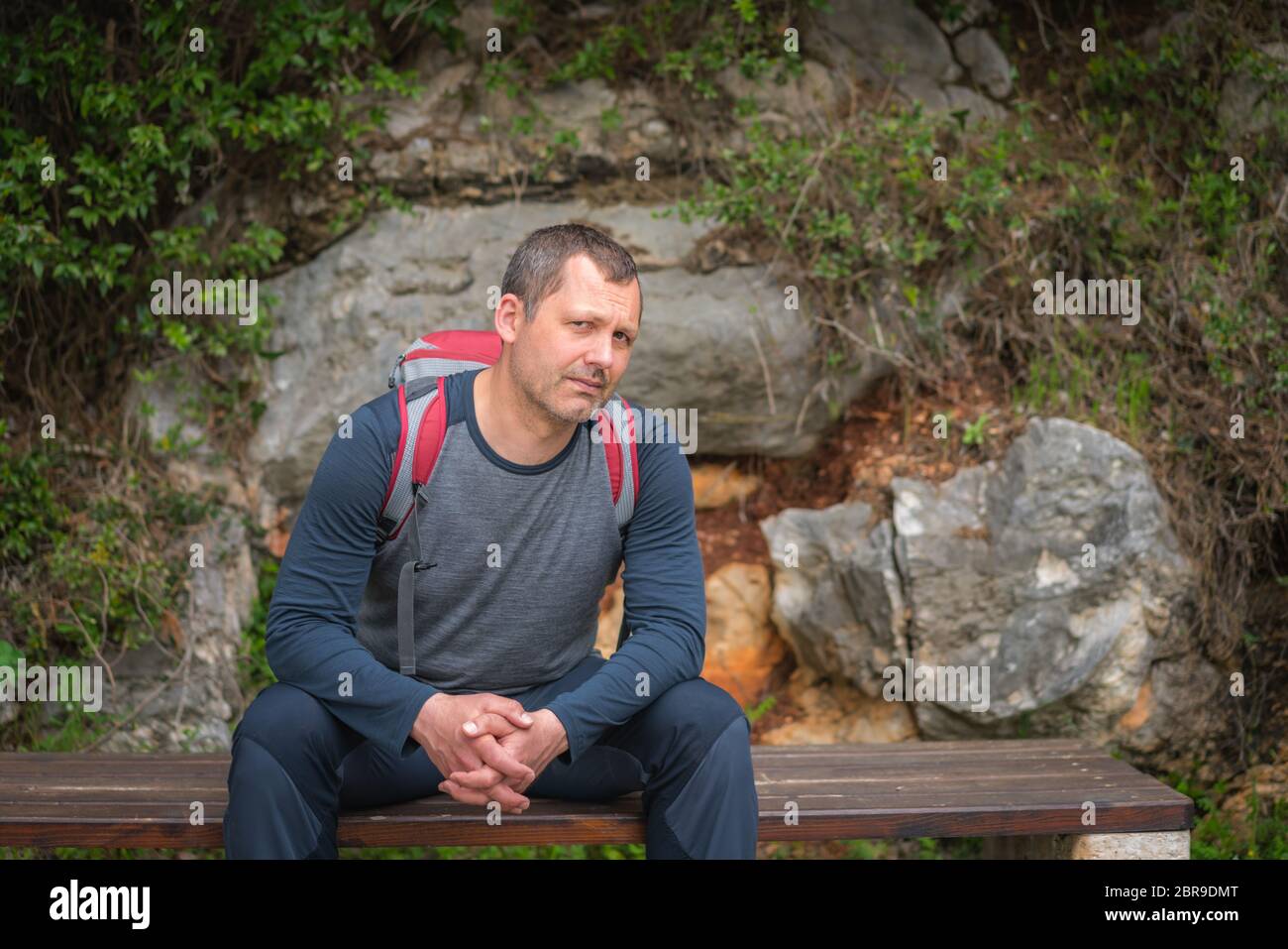 Homme de race blanche avec un sac à dos s'arrêter pour se reposer sur un banc en marchant sur un chemin dans une forêt sur un sentier côtier à Petrovac, Monténégro Banque D'Images