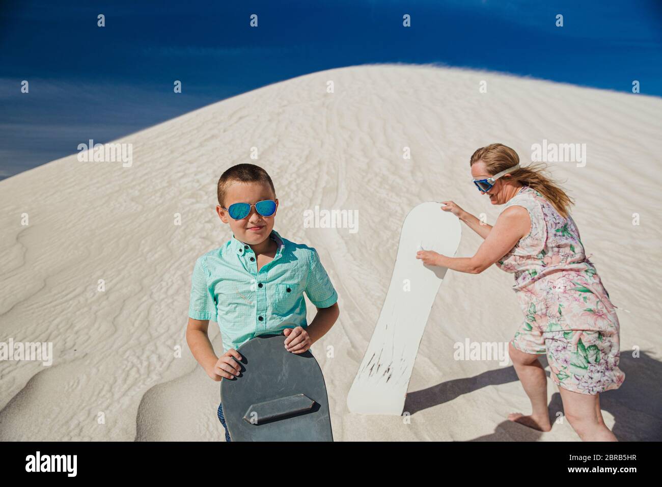 Portrait d'un petit garçon stadning sur une dune de sable à la Lancelin dunes de sable. Sa mère est debout derrière lui, jusqu'à la dune de sable avec un conseil de sable Banque D'Images