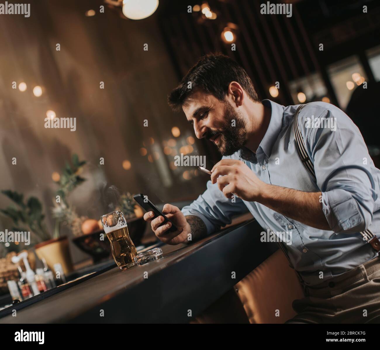 Un jeune homme boit de la bière et fume de la cigarette au pub Banque D'Images