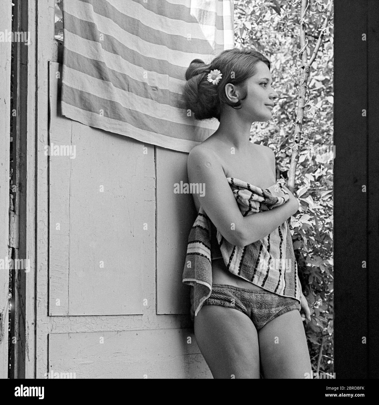 jeune jolie femme debout dans la porte maison rêvant de jour sur chaud ensoleillé jour portant bikini avec serviette années 1960 hongrie Banque D'Images