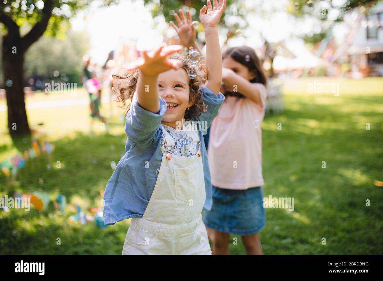 Les enfants en bas âge se tiennent à l'extérieur dans le jardin en été, jouant. Banque D'Images
