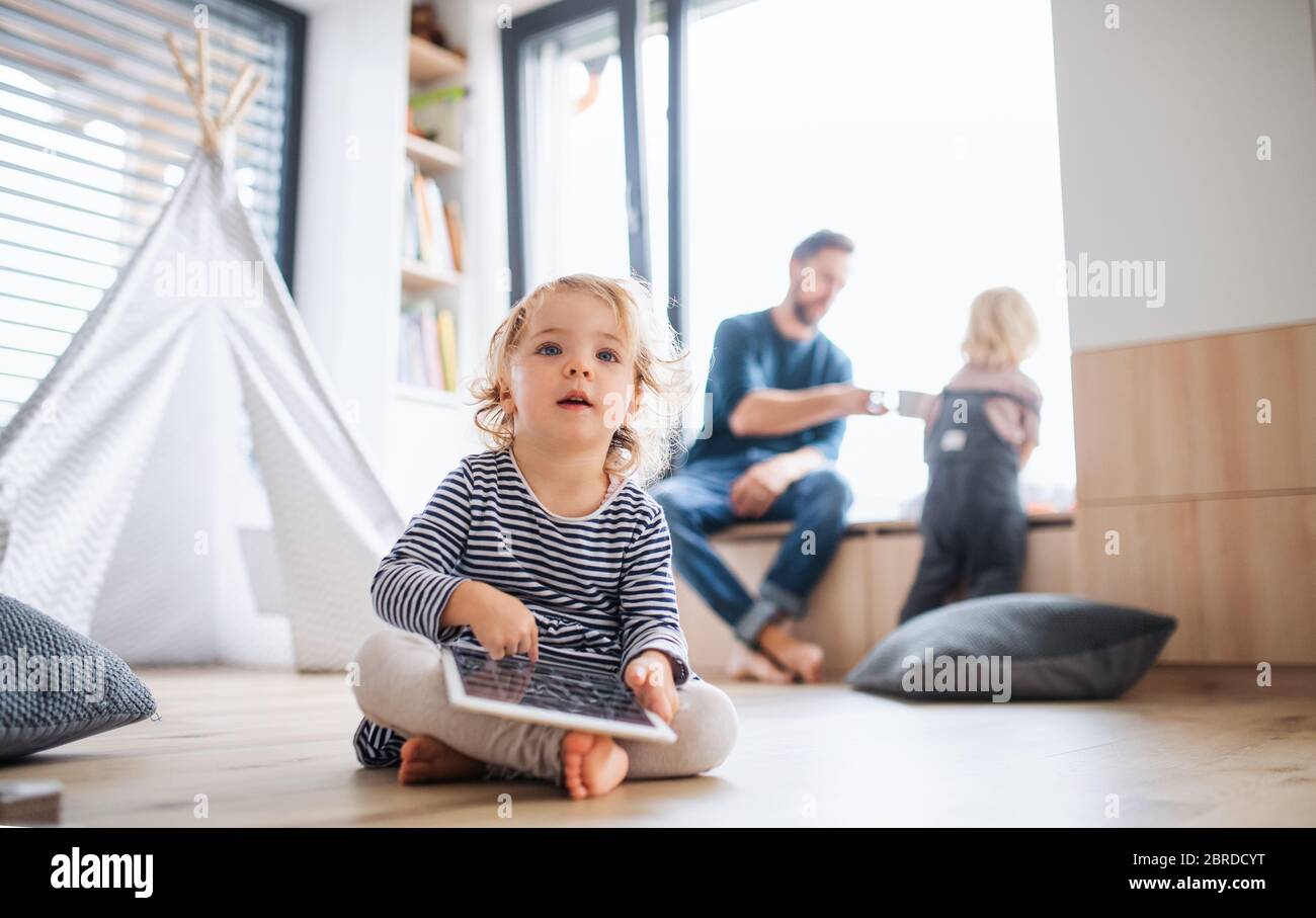 Petite fille assise à l'intérieur dans la chambre, avec une tablette. Banque D'Images