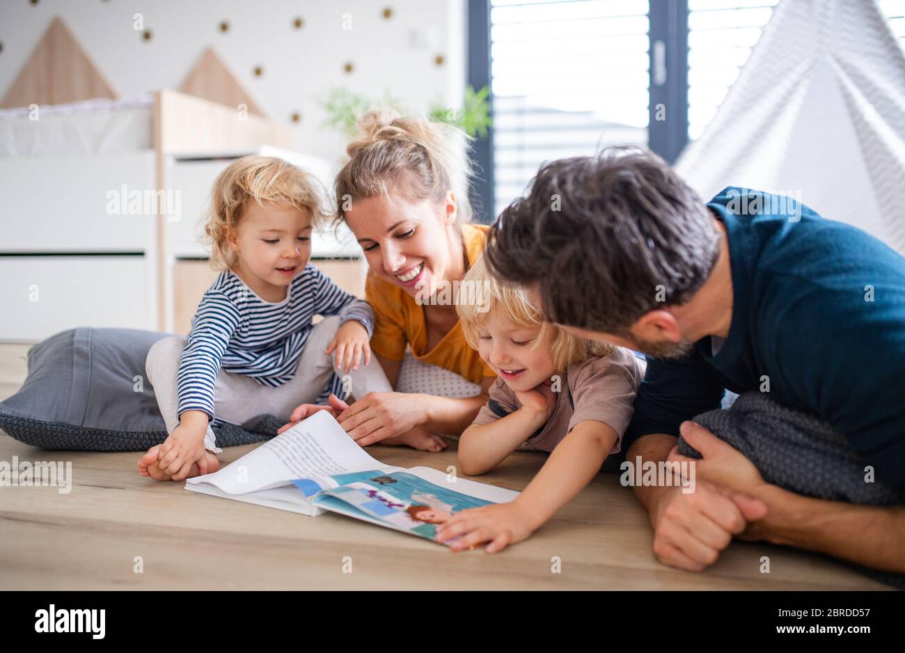 Une jeune famille avec deux petits enfants à l'intérieur dans la chambre à coucher lisant un livre. Banque D'Images