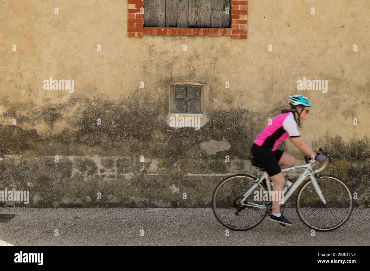 Femme cycliste passant la vieille maison de village à Rasteau dans le sud de la France Banque D'Images