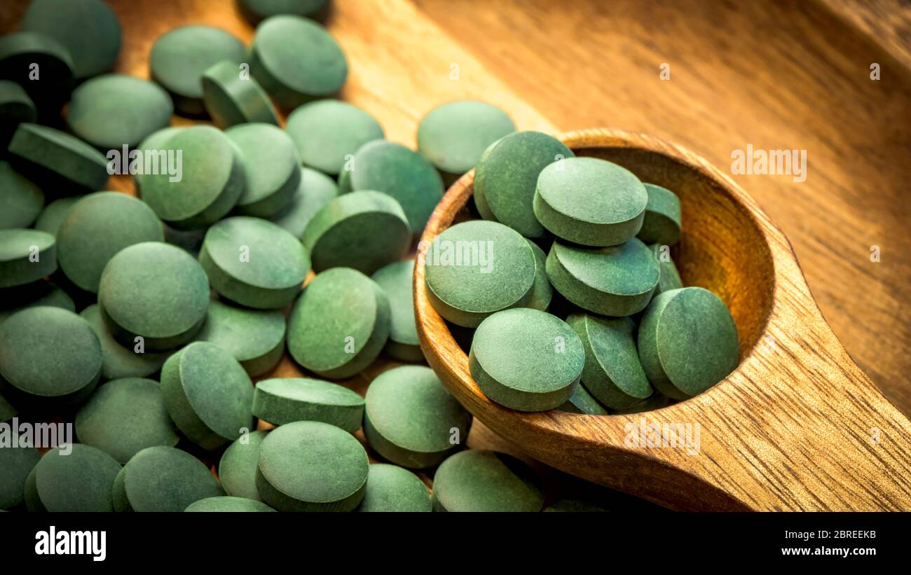 Algues vertes en comprimés - chlorelle, spiruline en cuillère en bois sur fond de bois - gros plan Banque D'Images