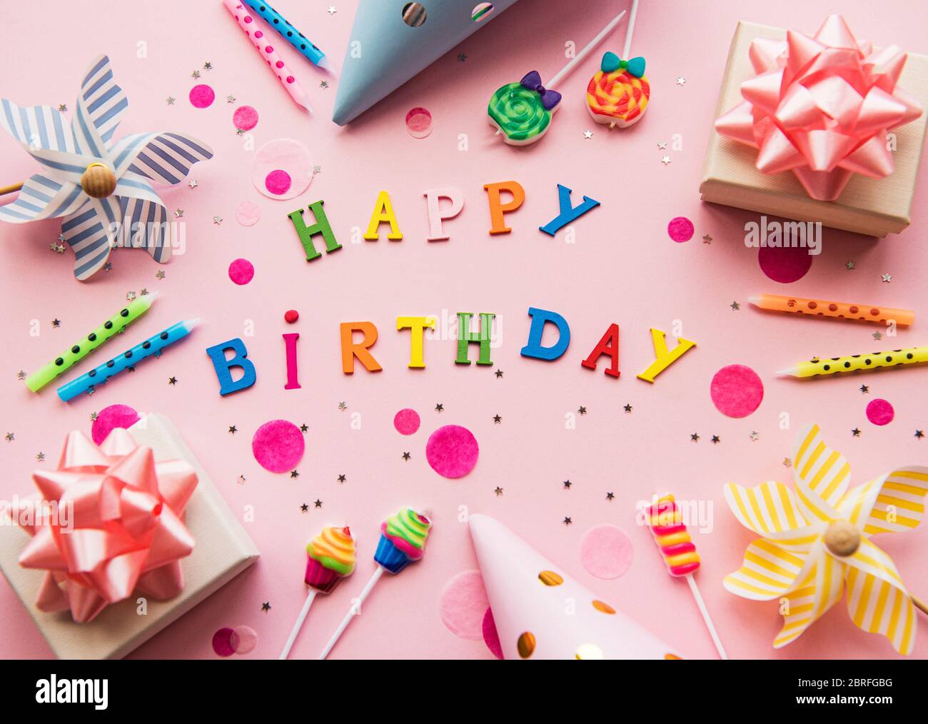 Texte Heureux anniversaire par lettres en bois avec des asseccories d'anniversaire, des bougies et des confettis sur fond rose Banque D'Images