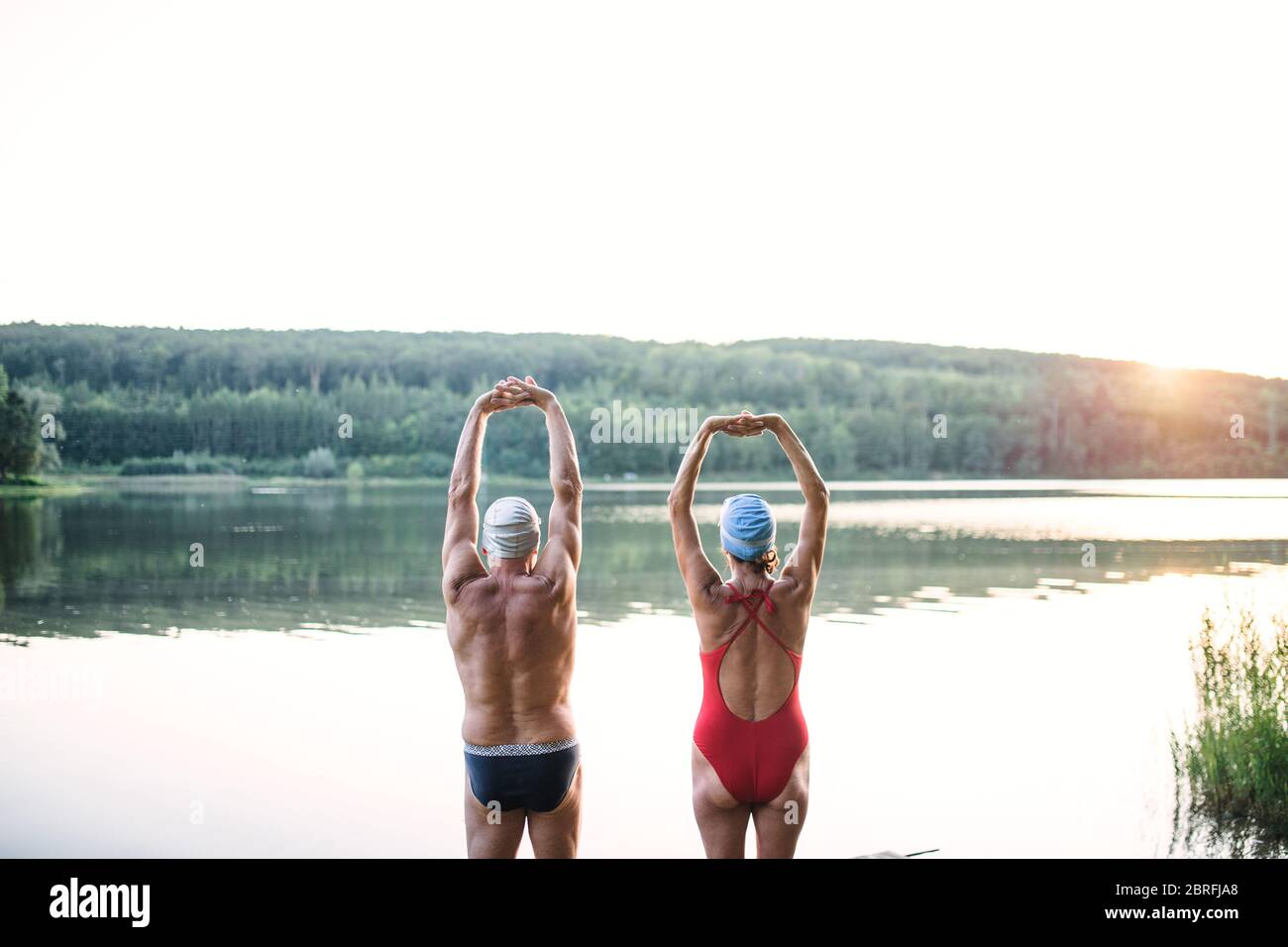 Vue arrière d'un couple senior en maillot de bain s'étendant au bord du lac à l'extérieur avant de nager. Banque D'Images