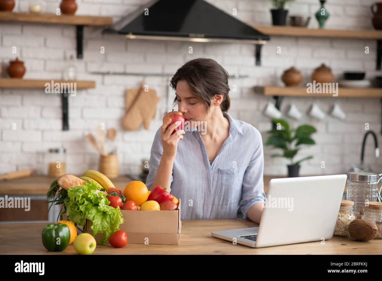 Fille en homowear gris assis à la table et sentant une pomme rouge Banque D'Images