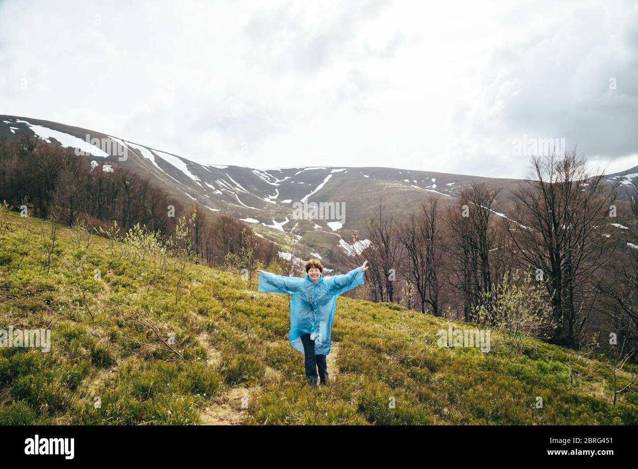 Happy smiling senior voyageur belle femme en bleu veste de pluie et un jean dans les montagnes, entourée de forêt, profiter du silence et l'harmonie de la nature Banque D'Images