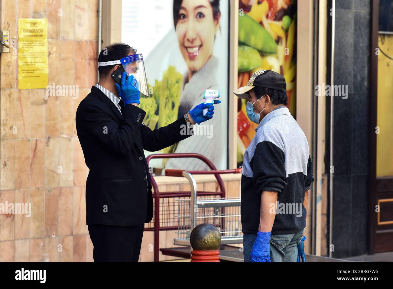 Londres, Royaume-Uni. 21 mai 2020. Un personnel de sécurité portant un masque facial et des gants analyse la température corporelle d'un client à l'entrée d'un supermarché pendant la pandémie du coronavirus. Le personnel de sécurité du supermarché Loon Fung de Chinatown prend des mesures préventives contre la propagation du COVID-19 en faisant passer les clients par un balayage de température avant de leur permettre d'accéder au magasin. Crédit : SOPA Images Limited/Alamy Live News Banque D'Images