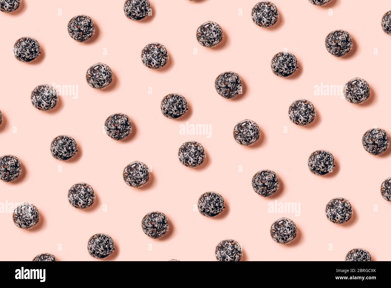 Boules d'énergie brute saines faites de fruits secs et de noix avec des copeaux de noix de coco, des graines de lin, des pistaches, du sésame. Motif sur fond rose. Banque D'Images