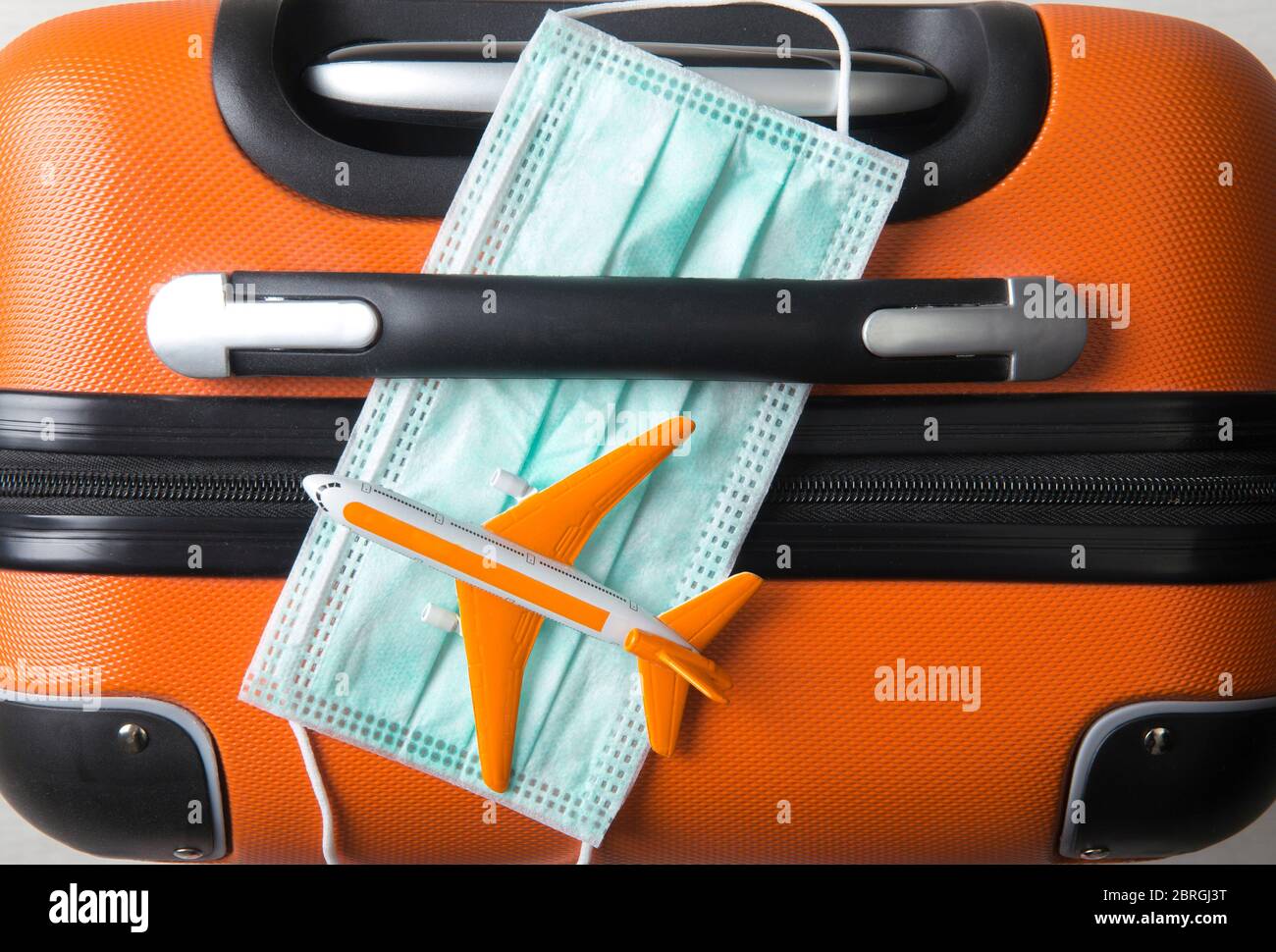 Vue à plat du masque médical avec figurine d'avion sur la valise à bagages. Concept de voyage pendant une épidémie de coronavirus. Année 2020. Banque D'Images