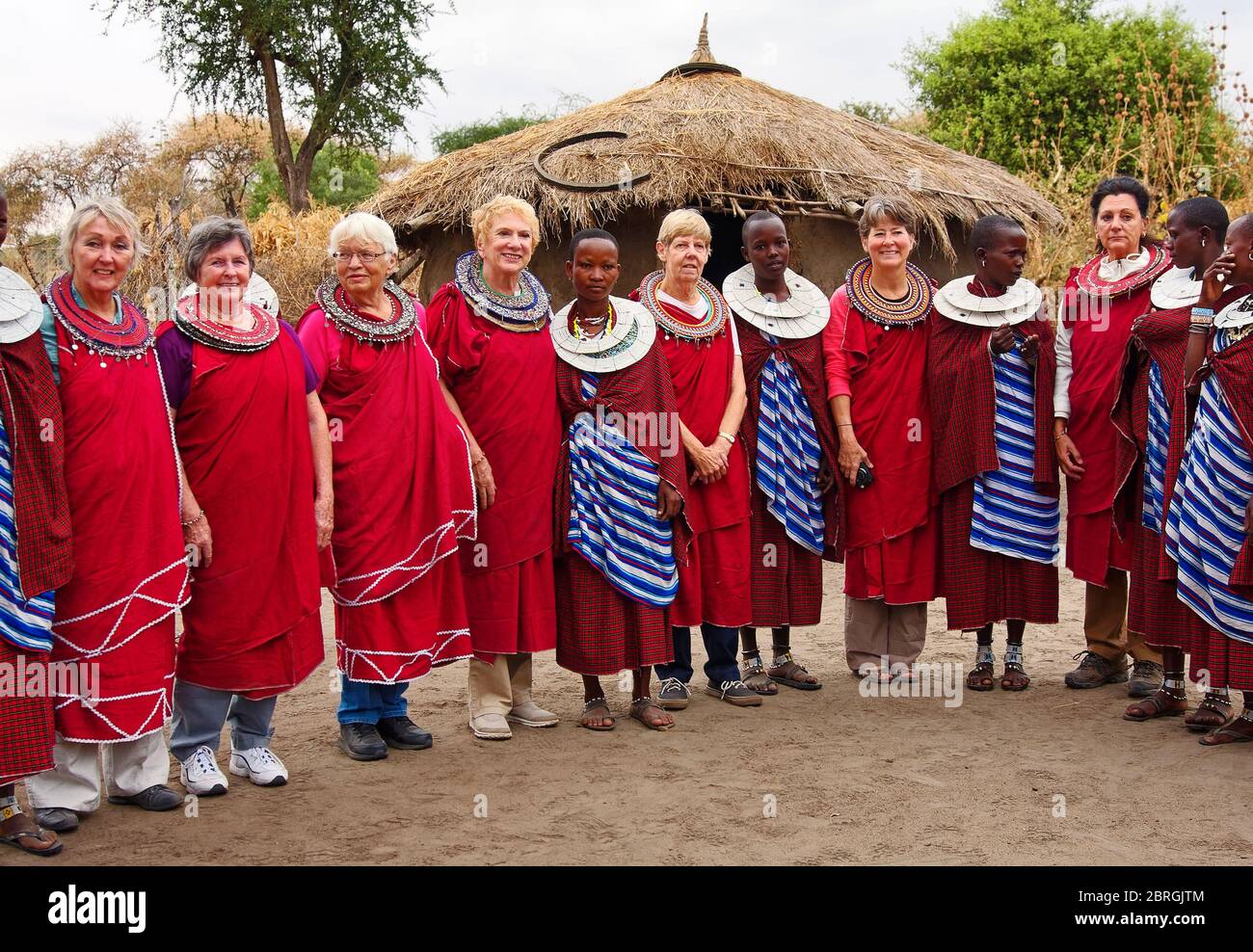 Maasai femmes, femmes visiteurs, touristes, safari, robe tribale rouge, cols à double perlé, toit en chaume maison, culture, portrait de groupe, Tanzanie; Africain Banque D'Images