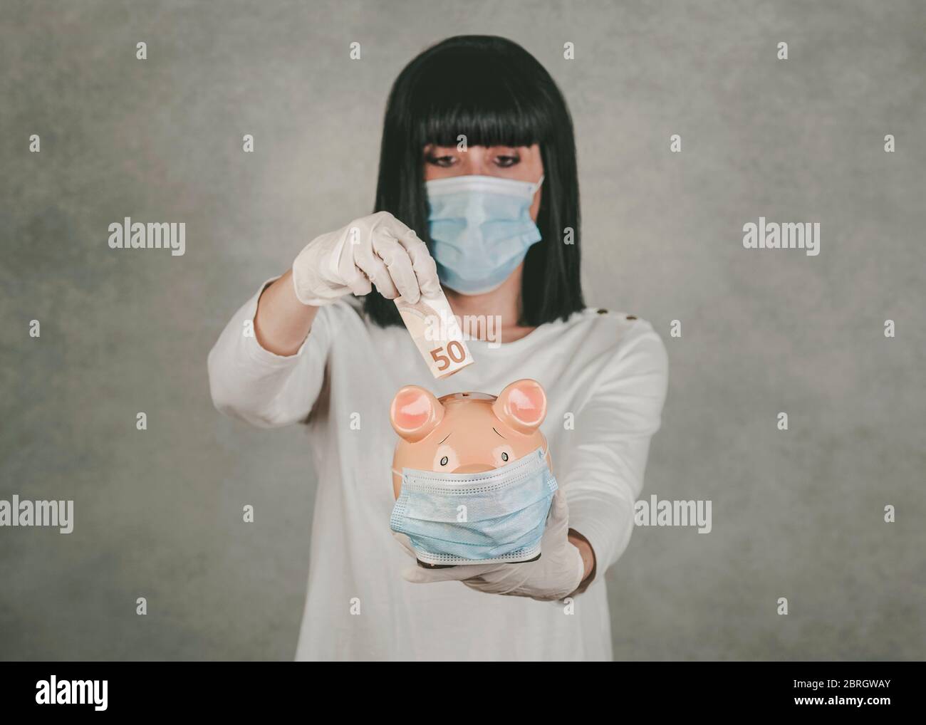 femme portant un masque médical pour le coronavirus avec une porcgybank sur fond gris Banque D'Images