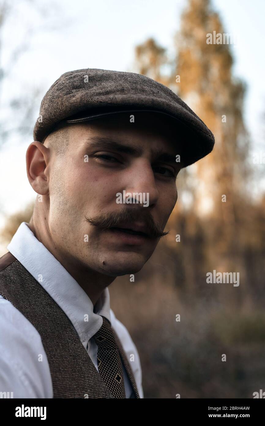 Portrait rétro des années 1920 d'un gangster anglais avec une casquette  plate. Fume une cigarette dans la rue Photo Stock - Alamy