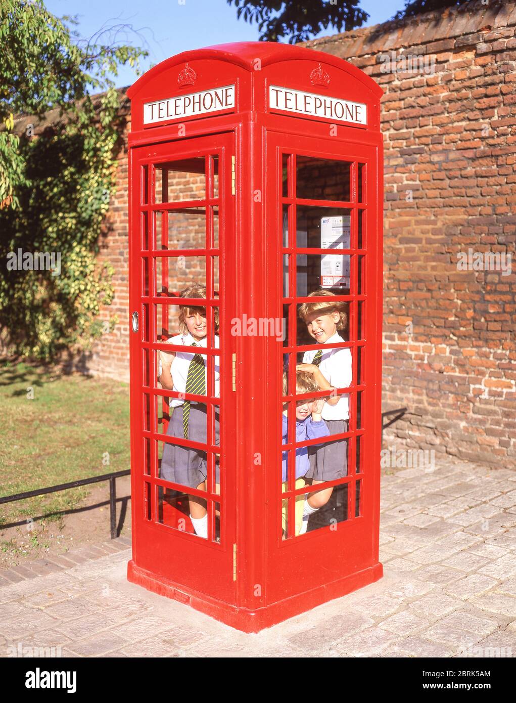 Enfants d'école se cachant dans un kiosque téléphonique rouge, Hampton, London Borough of Richmond upon Thames, Greater London, Angleterre, Royaume-Uni Banque D'Images