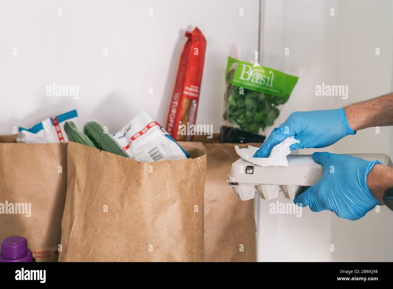 COVID-19: Est-il nécessaire de nettoyer vos produits livrés à la maison. Homme en quarantaine essuyant l'emballage en carton avec des lingettes désinfectantes après avoir fait des achats ou reçu des sacs de livraison en ligne. Banque D'Images