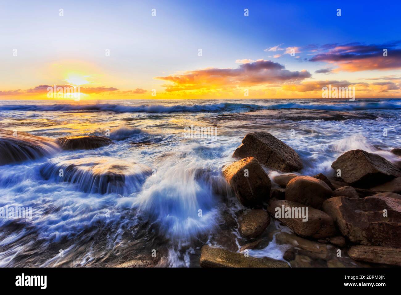 Courant de puissantes vagues qui frappent les rochers de grès de la plage de Bungan, sur la côte Pacifique de Sydney, au lever du soleil. Banque D'Images