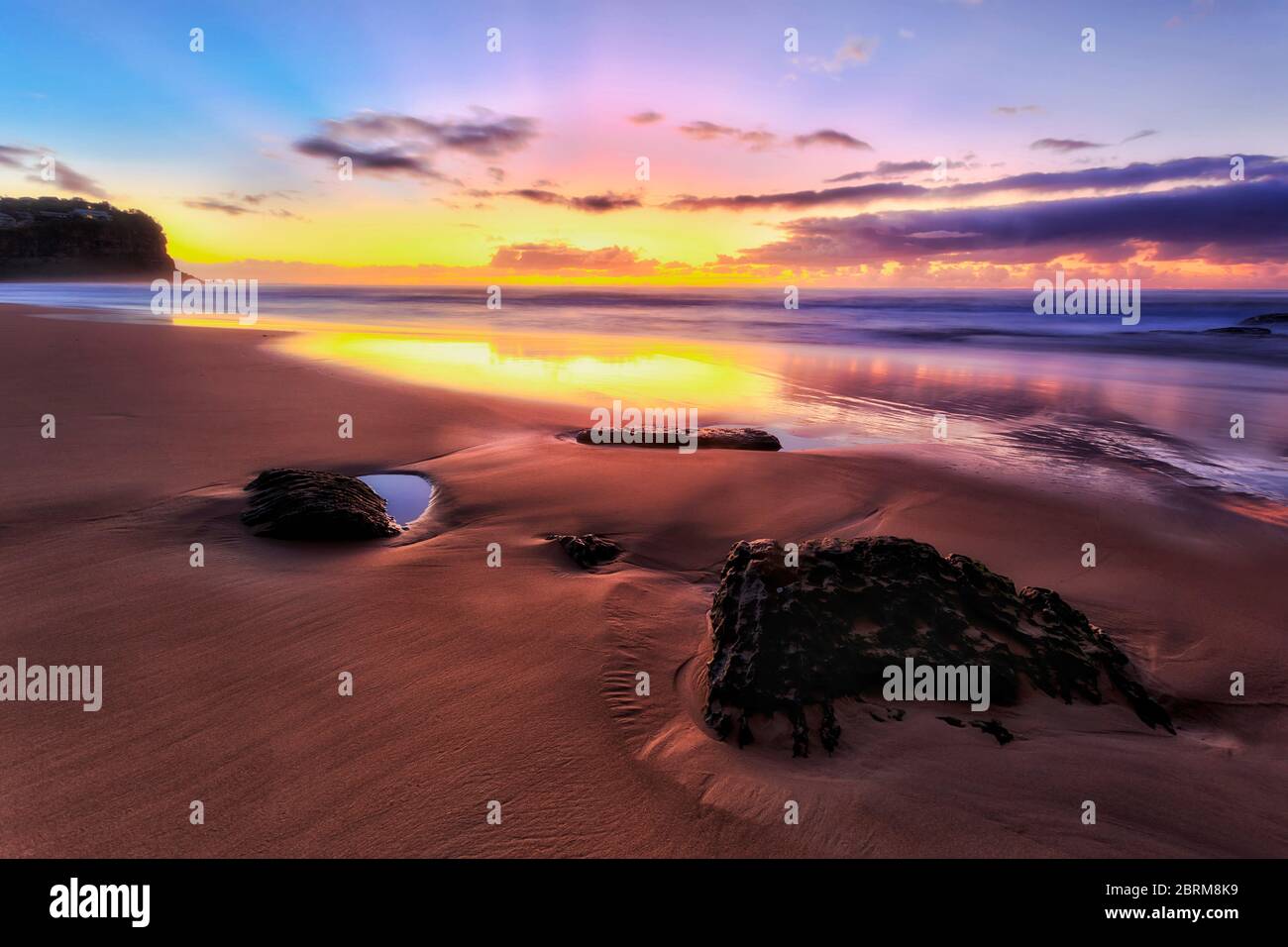 Du sable lavé autour des rochers de grès sur la plage de Bungan à Sydney au lever du soleil, contre les vagues de l'océan qui rescaptent la lumière du soleil. Banque D'Images