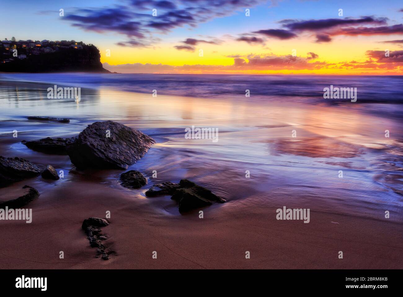 Sable humide autour des rochers de grès à Bungan Beach de Sydney au lever du soleil avec reflet de la lumière du soleil. Banque D'Images