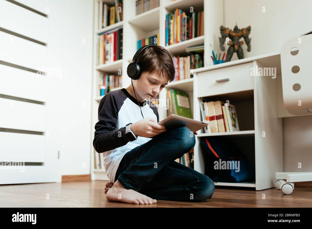Un garçon qui s'agenouille apprend sur une tablette numérique à la maison. Un jeune étudiant fait ses devoirs seul. Banque D'Images