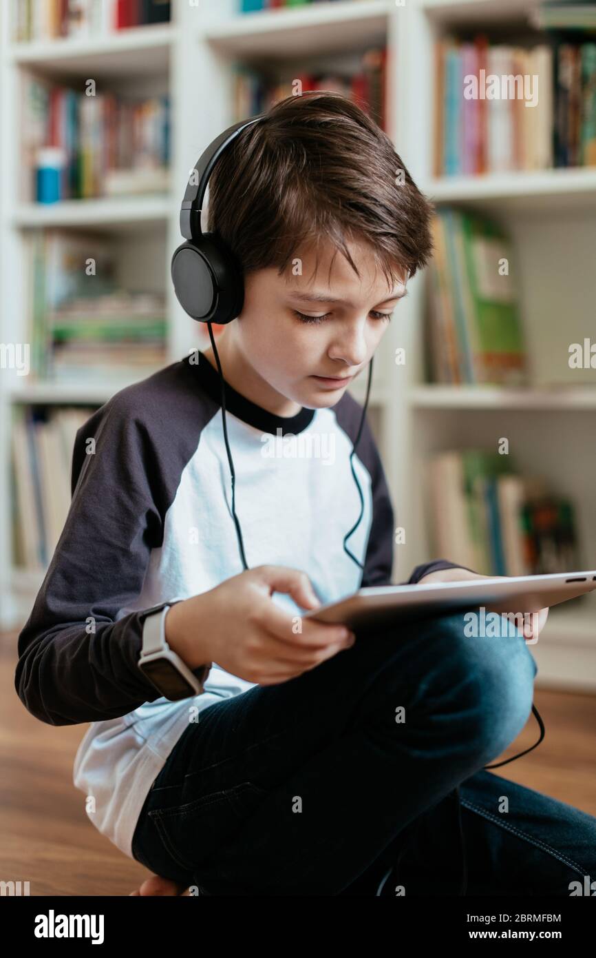 Garçon assis sur le sol apprenant sur une tablette numérique à la maison. Jeune étudiant apprenant en ligne seul. Banque D'Images