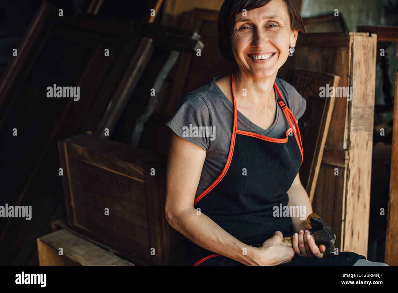Charpentier femelle heureux avec marteau dans l'atelier souriant à la caméra Banque D'Images