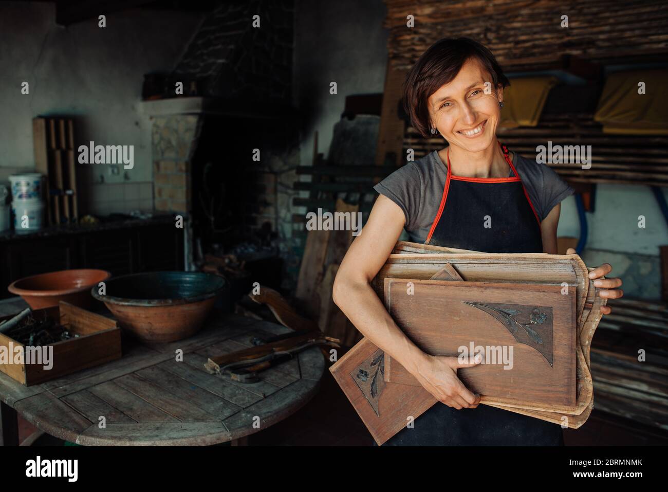 Une femme souriante tenant des panneaux de bois dans un atelier Banque D'Images