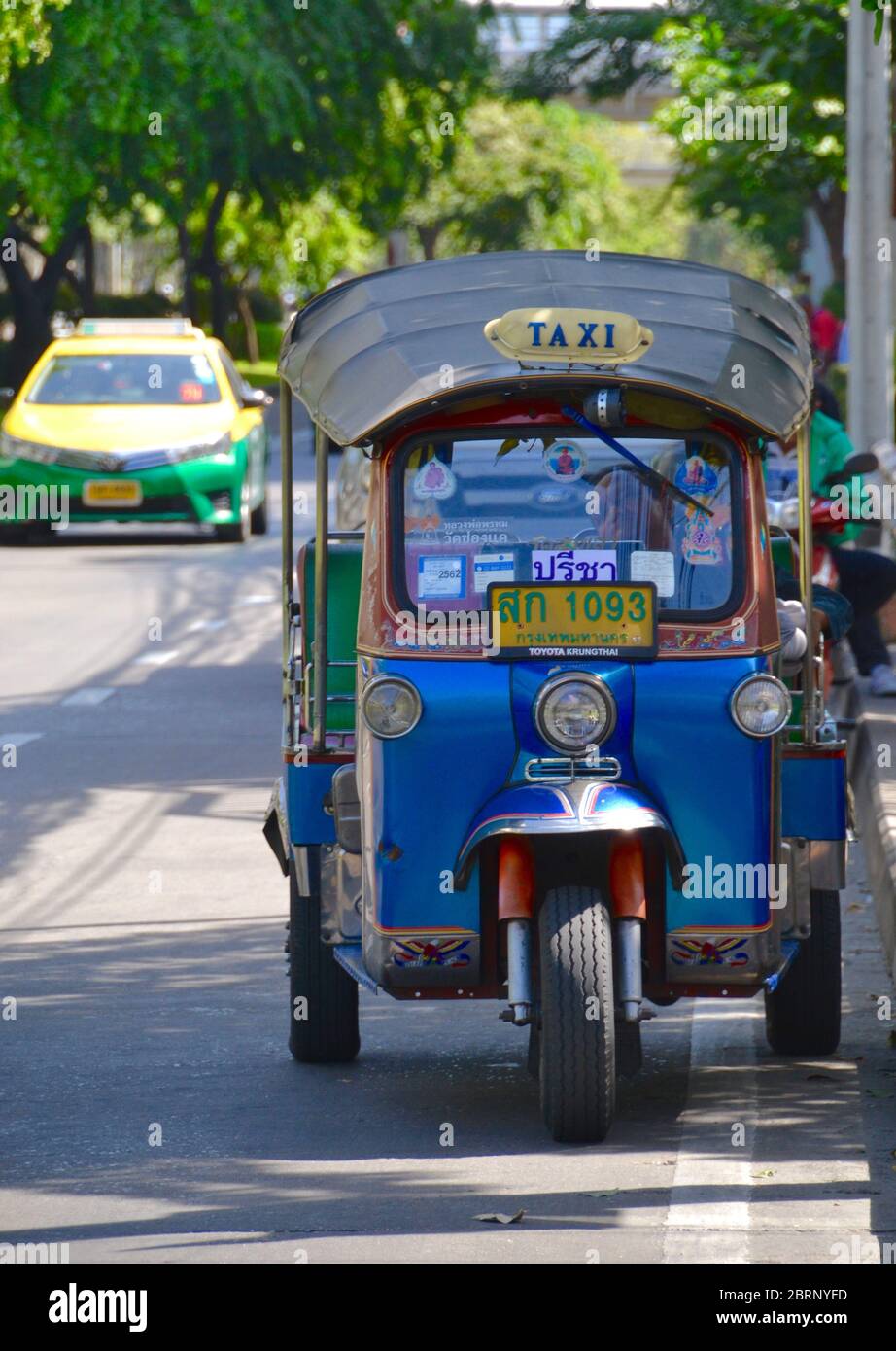Contraste entre l'ancien et le nouveau Bangkok avec un tuk-tuk décoré en premier plan et un taxi moderne vert et jaune en arrière-plan Banque D'Images