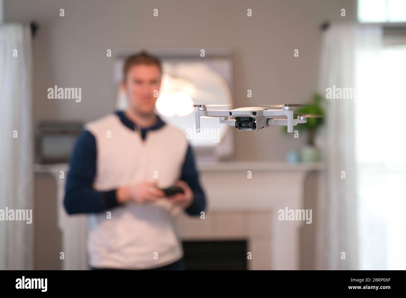 Drone volant à l'intérieur avec pilote visible en arrière-plan. Vol de drone amateur. Utilisateur portant un sweat-shirt volant drone à l'intérieur de la maison par temps froid. Blanc dr Banque D'Images