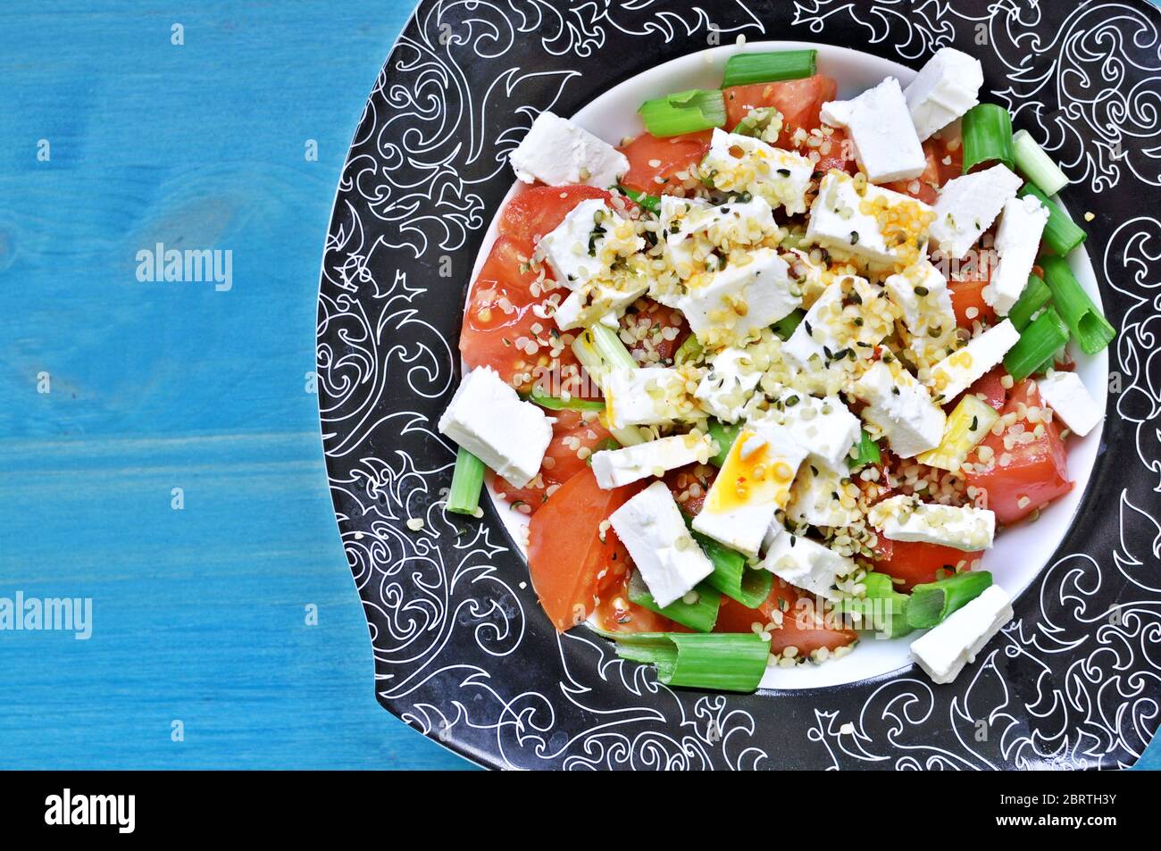 Sur une assiette de salade de tomates et d'oignons verts avec du fromage et du chanvre sur fond bleu. Copier le texte d'espace. Banque D'Images