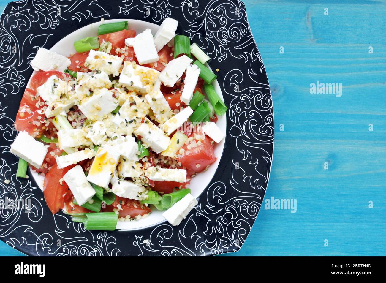 Sur une assiette noire sur fond bleu, garnir de tomates et de salade d'oignons verts avec du fromage et du chanvre. Copier le texte d'espace. Banque D'Images