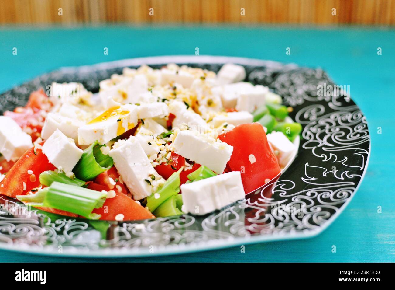 Salade de tomates et d'oignons verts avec fromage et chanvre sur une assiette sur fond bleu. Banque D'Images