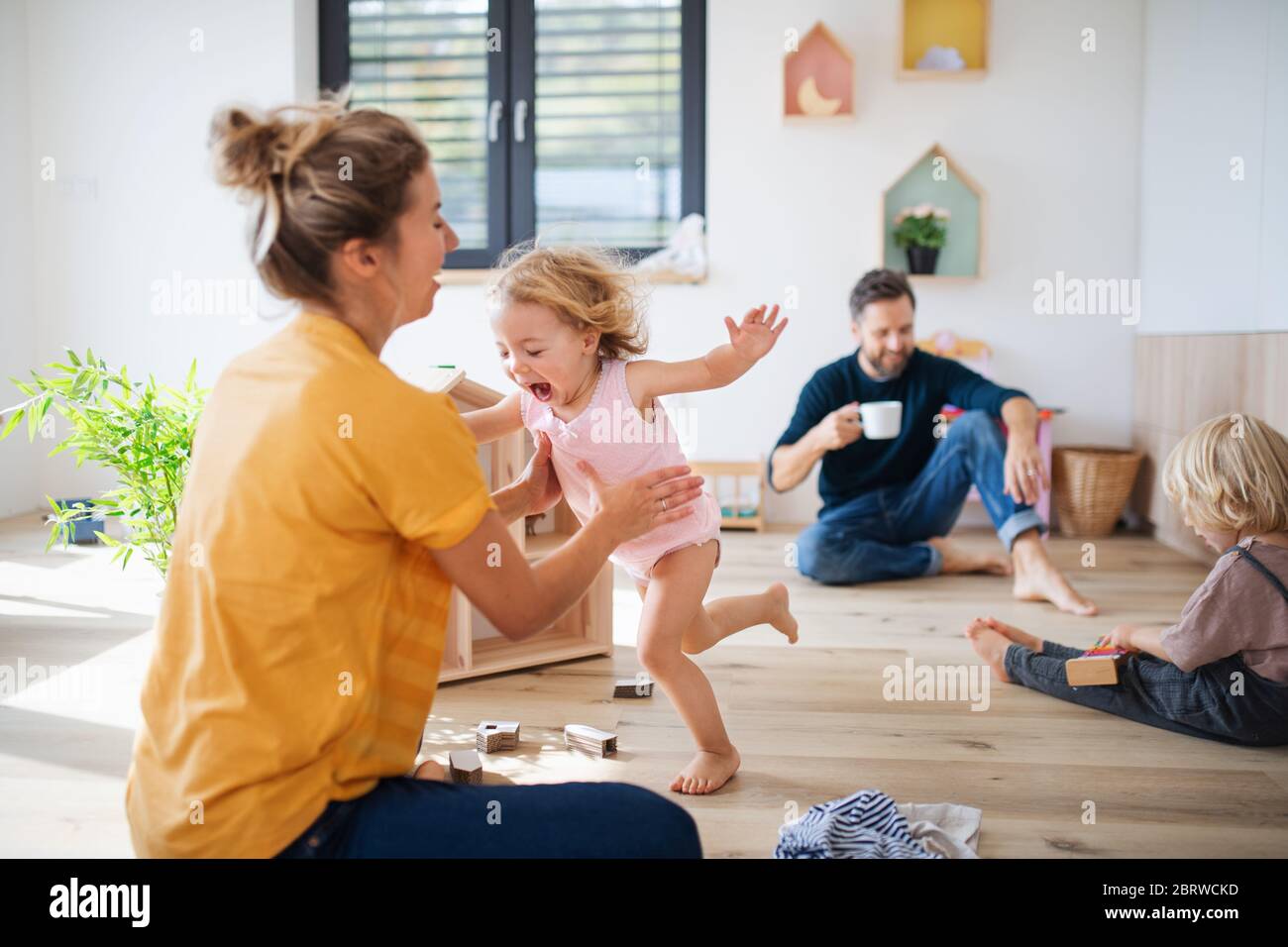 Jeune famille avec deux petits enfants à l'intérieur dans la chambre à coucher jouant. Banque D'Images
