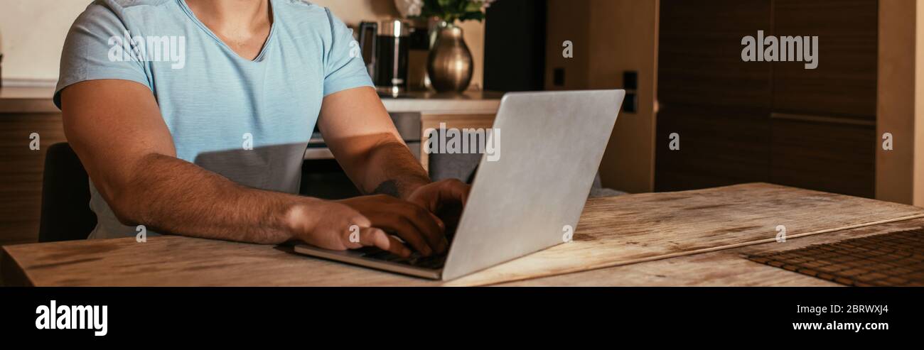 vue rognée d'un homme de course mixte indépendant travaillant avec un ordinateur portable sur la cuisine pendant l'auto-isolation, en-tête de site web Banque D'Images