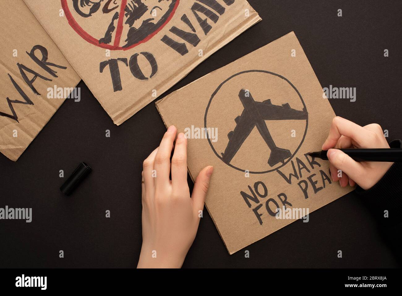 vue rognée de la femme à dessiner avec le lettrage sans guerre pour la paix et l'avion sur fond noir Banque D'Images