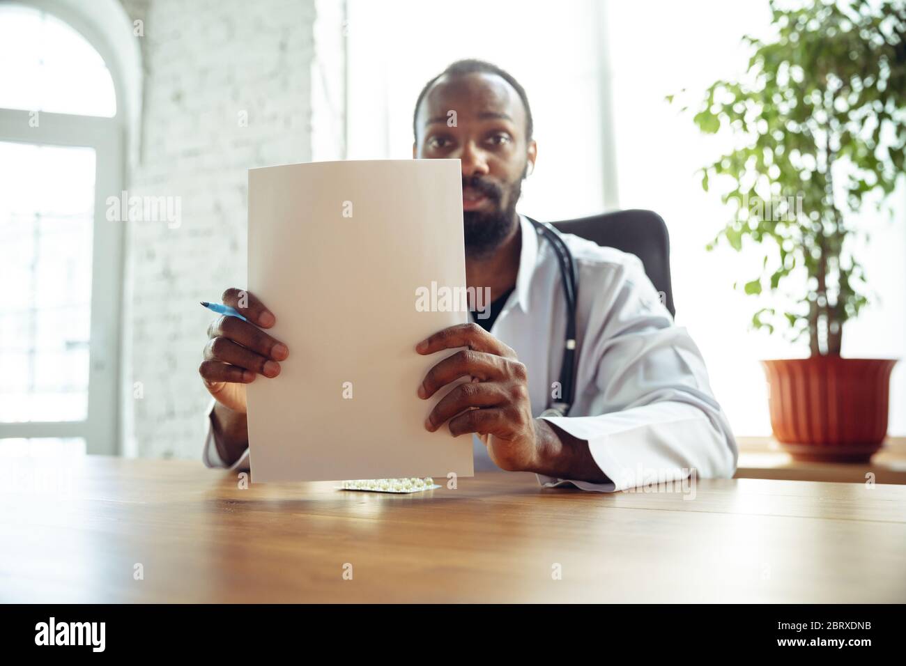 Médecin conseillant le patient en ligne avec un ordinateur portable. Médecin afro-américain pendant son travail avec les patients, expliquant les recettes pour la drogue. Travail quotidien pour la santé et la vie sauvant pendant l'épidémie. Banque D'Images