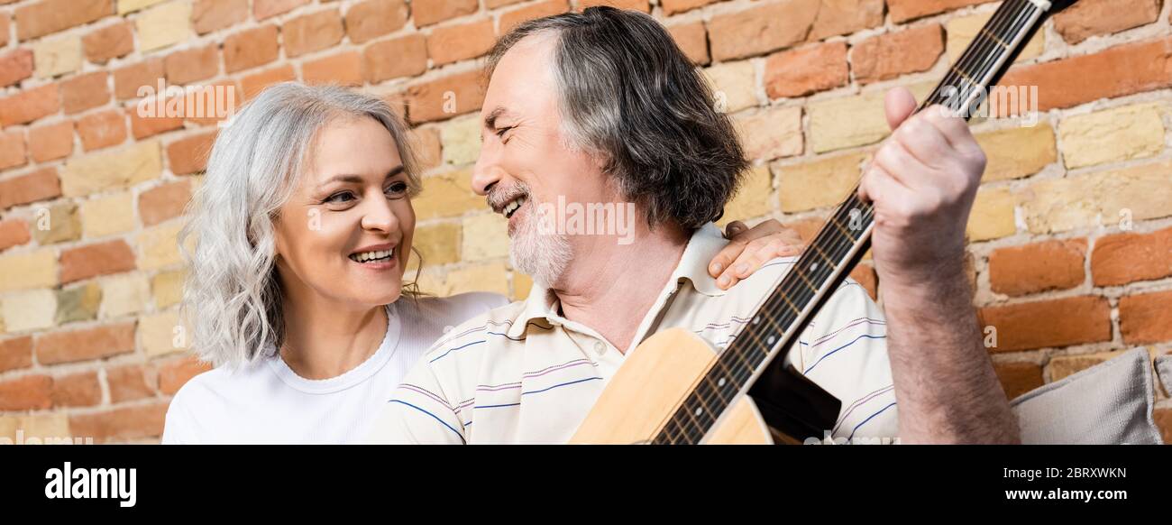 photo panoramique d'un homme barbu et mature jouant de la guitare acoustique près d'une femme souriante Banque D'Images