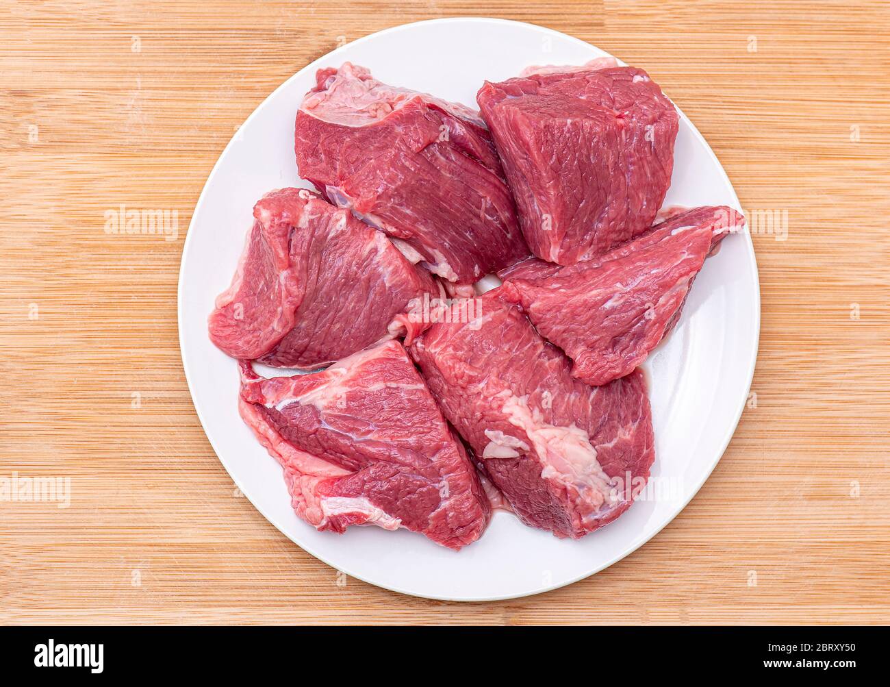 Gros morceaux de bœuf cru pour barbecue ou viande de goulash sur plaque blanche, vue du dessus Banque D'Images