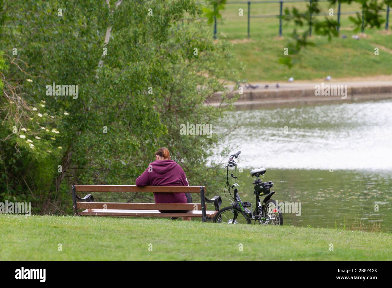 ECO-Stepper E-bike sur le stand tandis que le motard féminin est assis sur un banc de parc à Abington Park, Northampton, Angleterre, Royaume-Uni. Banque D'Images