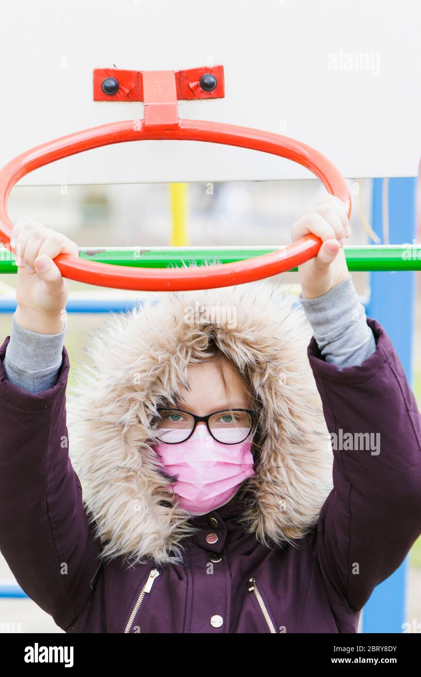 Portrait d'une fille dans un masque médical et des lunettes à l'aire de jeux. Banque D'Images