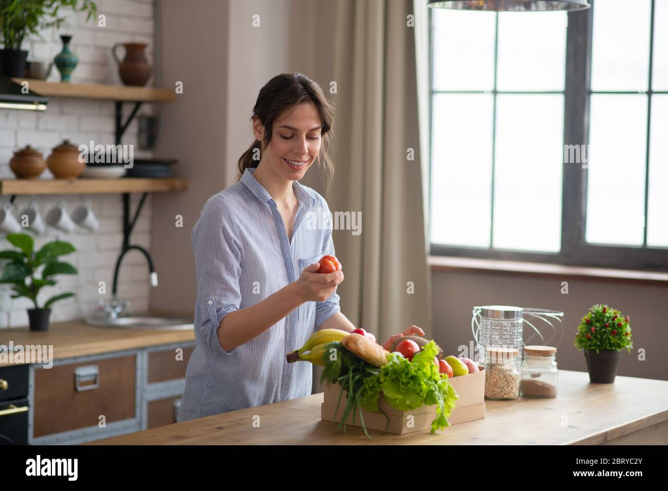 Fille en forme de femme grise debout dans la cuisine et tenant un poivron rouge et souriant Banque D'Images