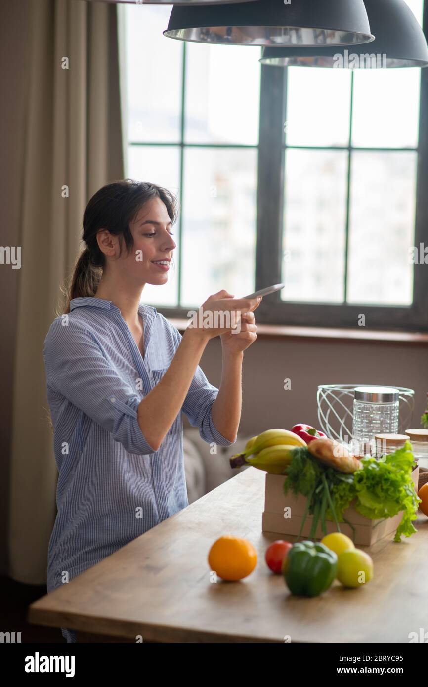 Fille en casque d'intérieur gris assise dans la cuisine avec un smartphone et faire des photos Banque D'Images