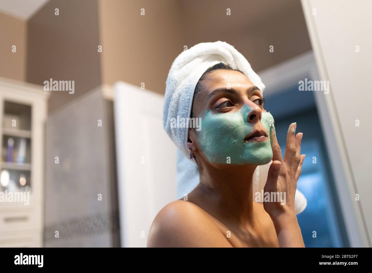 Femme debout dans la salle de bains, appliquant le masque de visage après le bain. Banque D'Images