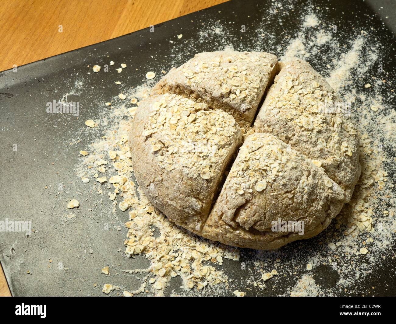 Une partie de pâte à pain au soda coupée avec une croix recouverte d'avoine sur une plaque de cuisson farinée prête pour le four Banque D'Images