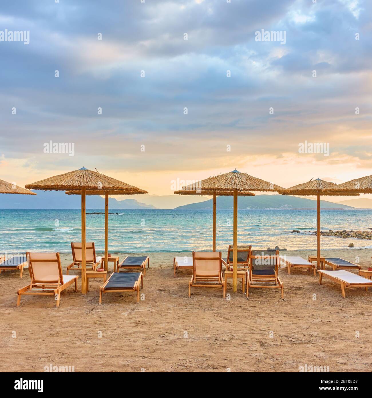 Vue pittoresque sur la plage avec des rangées de parasols en paille au coucher du soleil Banque D'Images